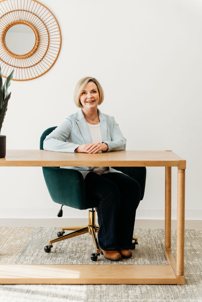 Smiling woman sitting at a wooden desk in a bright office space.