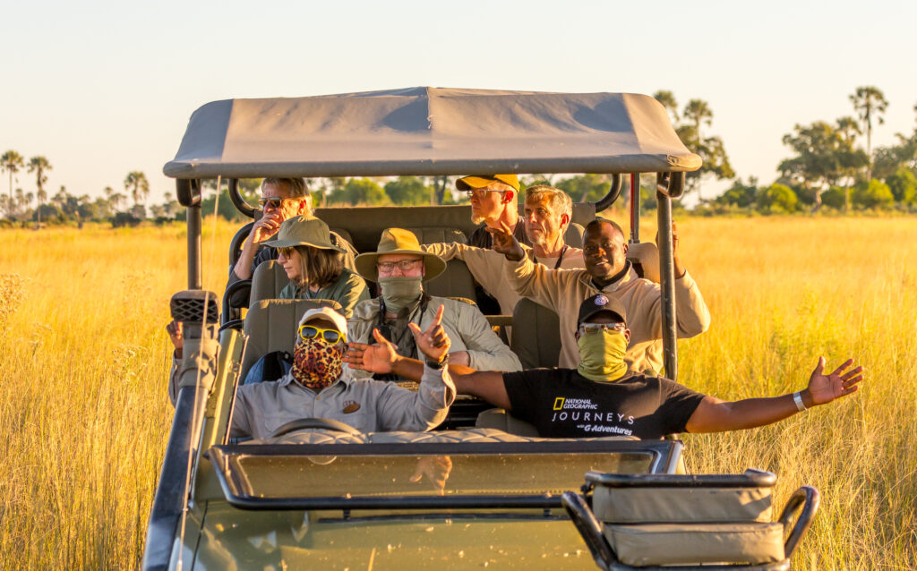 Group enjoying a safari ride waving from a jeep at sunset.
