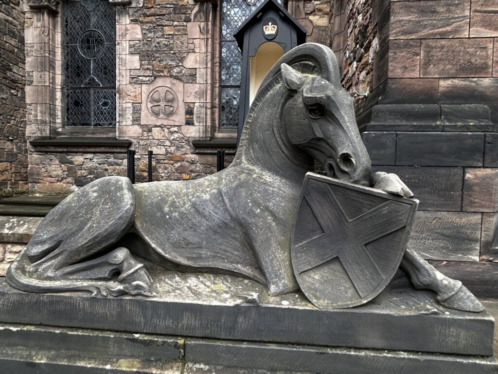 Stone ram sculpture holding a shield with a cross symbol.