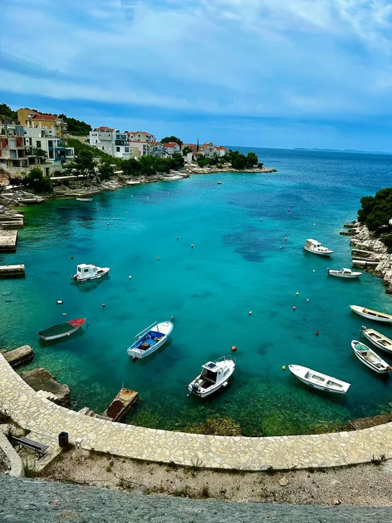 Boats anchored in a serene turquoise bay surrounded by rocky cliffs and houses.