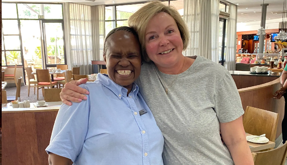 Two women smiling and hugging indoors.