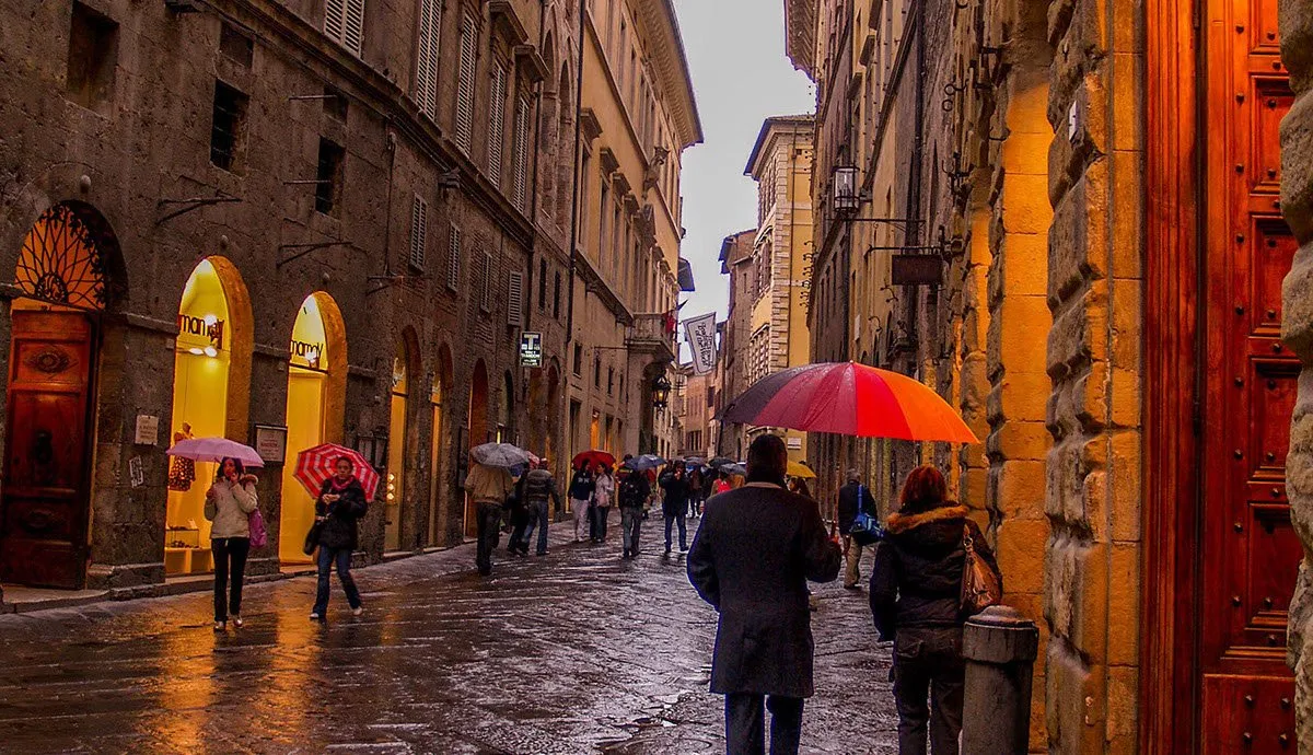 People walking with umbrellas on a rainy city street at dusk.